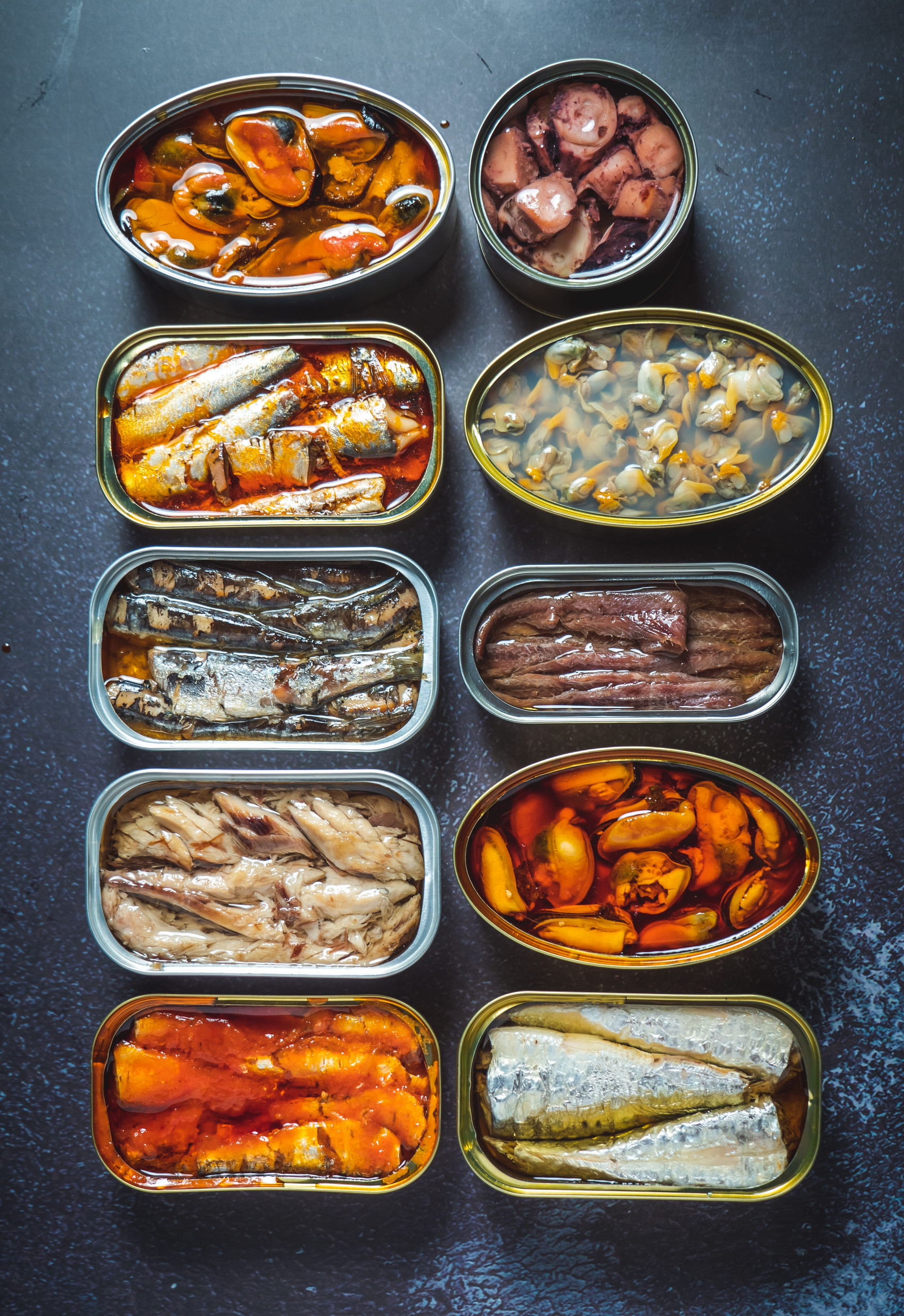 Preserve cans with different products, fish and seafood, natural or pickled, open on a dark table