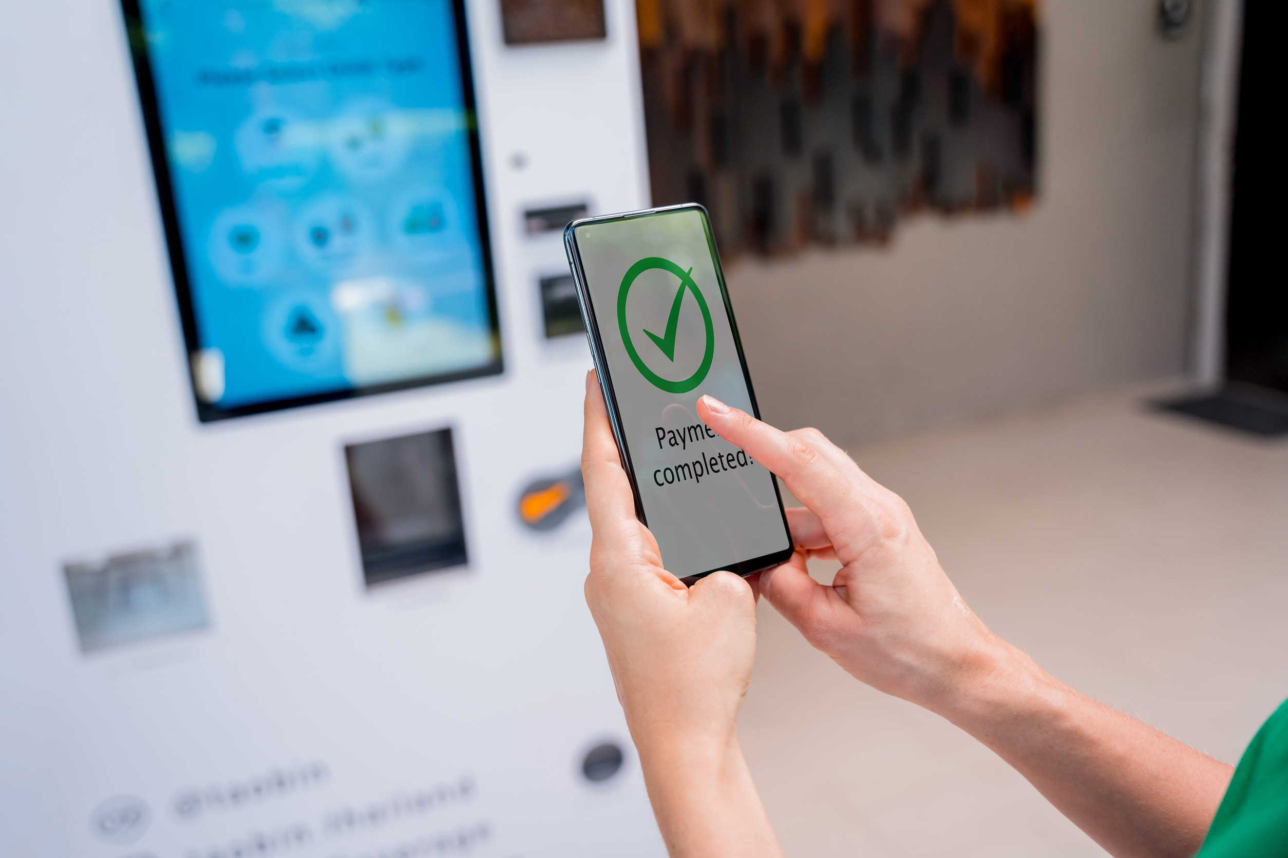Young woman paying for coffee at vending machine using contactless method of payment