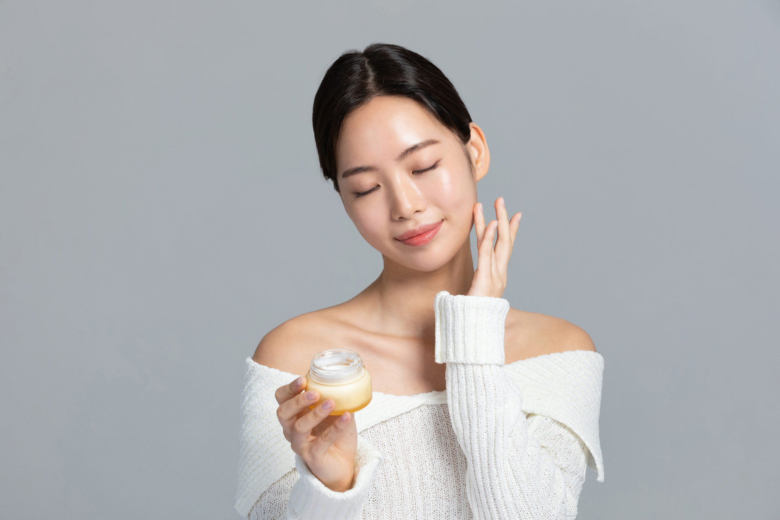 beautiful young Korean Asian woman portrait studio photo in winter skin beauty and cosmetics concept__holding a nutritional cream